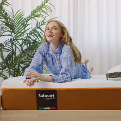 A woman is lying on a Valmori S-Shape Foam Mattress (Medium) features the Valmori Logo on the side of the mattress