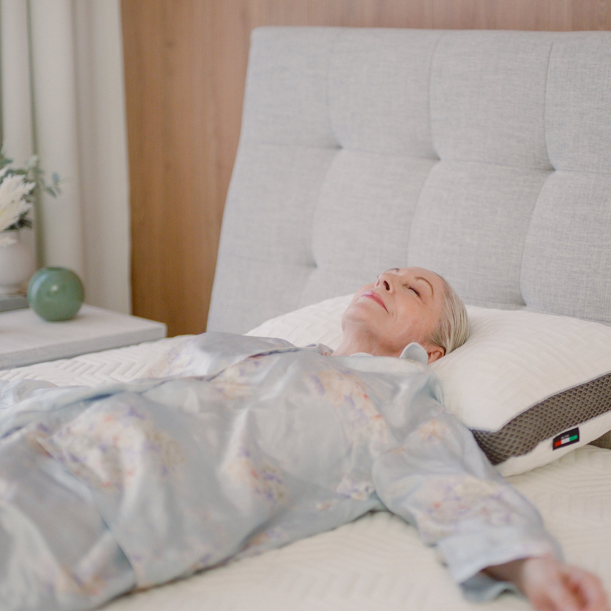 A person lying on a Hybrid Mattress Ⅱ (Medium) bed with a grey upholstered headboard.