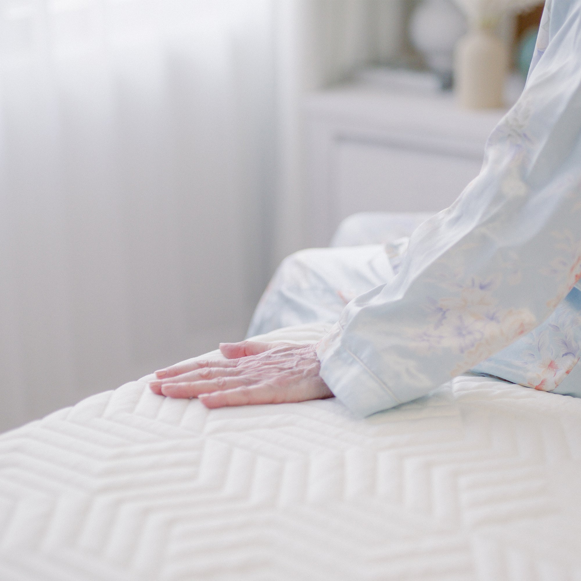 A close-up of a hand resting on a Valmori Medium Hybrid Mattress Ⅱ with a textured pattern, with the person wearing light-colored, floral-patterned pajamas.