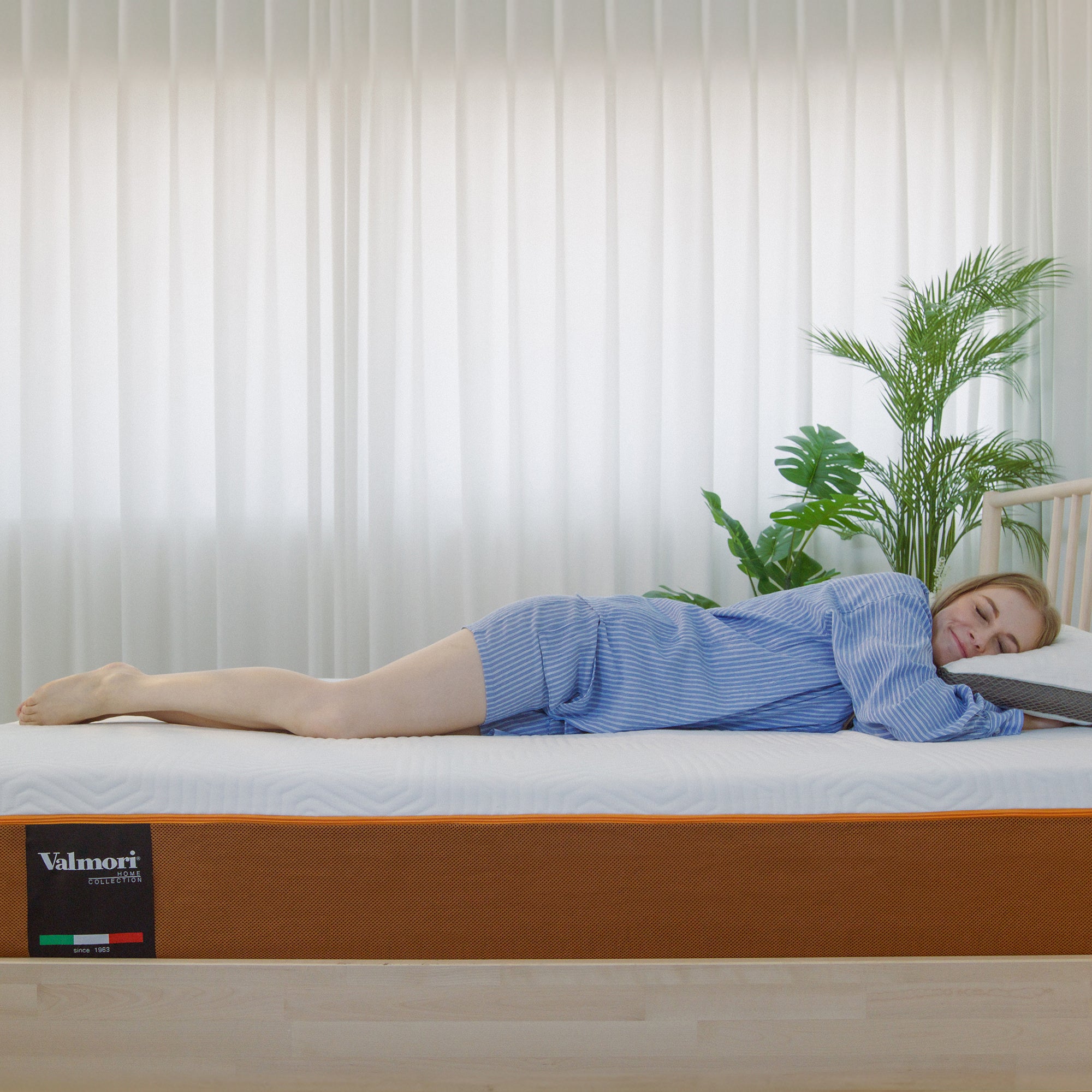 A lady lying on their side on a Valmori S-Shape Foam Mattress Ⅱ (Medium) in a room with white curtains and green plants.